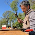 Arbeiten am Bootssteg: Fixierung neuer Holzplanken mit einer Schraubzwinge und Hammer.