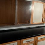 Zwei Küchen-Hängeschränke mit gemusterten Glasscheiben und zwei Holzschränke fertig montiert über einer dunklen Arbeitsplatte im Keller.
