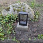 Modern montierte LED-Pollerleuchte aus Edelstahl auf einem Betonfundament im Gartenbeet vor einem Findling.